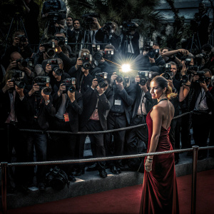 Keira Knightley at Cannes Film Festival. Wearing an elegant red dress, poses confidently on the red carpet surrounded by flashing cameras.