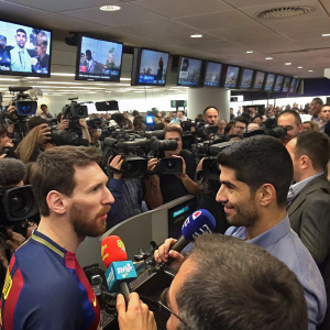 Lionel Messi and Luis Suarez during a bustling press conference. A large crowd of reporters and photographers surround them.
