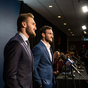 Jonathan Huberdeau and Vincent Trocheck, both in formal suits, at a post-game press conference. Press row behind them.