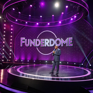 Steve Harvey's Funderdome show. Circular black stage. Illuminated logo. Bright purple lighting. Photo