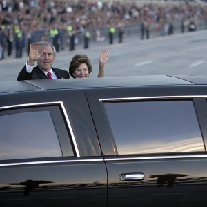 George W. Bush and Laura Bush, waving from a sleek black limousine. A sea of spectators in the background.