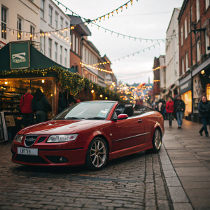 A Saab 93 2.0T Aero Convertible in cherry red, parked amidst a bustling street market. Festive decorations adorn the shops behind.