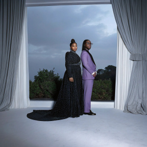 Tiffany Haddish and Law Roach at the Met Gala. Tiffany in a black polka dot gown, Law in a purple tailored suit. Greenery and curtains backdrop