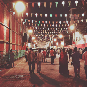 Vibrant night scene of a bustling street in Kolkata during Durga Puja. Colorful lights and banners decorate the area. Diverse crowd of locals and tourists walking along the pathway, immersed in the festive atmosphere. Urban setting comes alive with the festive spirit