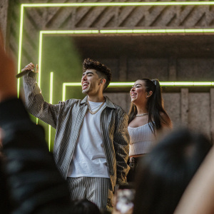 Mario Bautista and Caeli, flashing smiles, against neon-lit backdrop. Entertaining crowd at Nickelodeon Kids' Choice Awards Mexico, Auditorio Nacional.