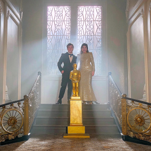 Matthew Xia and Vikki Stone at the London Theatre Awards. Wearing elegant gowns and suits, posing with a golden trophy in a glamorous setting.