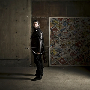 Hanzo, the legendary Overwatch hero, stands against a vibrant, colorful comic book backdrop. His detailed Asian-inspired hairstyle and facial hair are prominent. Wearing a sleek, black outfit.