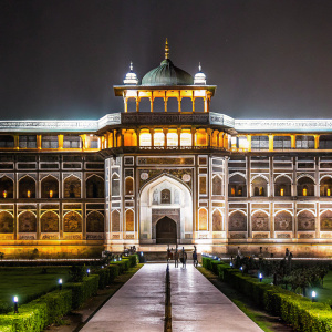 Photograph of Jahangiri Mahal. Majestic red sandstone palace within Red Fort of Agra, India. Ornate facade with numerous arches and a prominent central entrance. Intricate details and rich earth tones. Surrounded by lush greenery and manicured lawns.