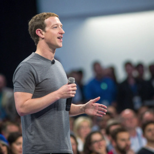 Mark Zuckerberg in a casual gray t-shirt, presenting at tech conference. Audience blurred in background.