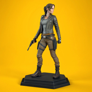 A detailed action figure of Lara Croft, featuring a sleek gray jacket, utility belt, brown cargo pants, and weapon in hand. Set against a bright yellow background, the figure stands on a black base.
