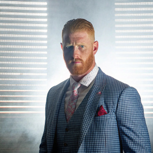 Ben Stokes, England's cricketer, intense gaze, styled beard and hair. Wearing formal attire. Gray backdrop.