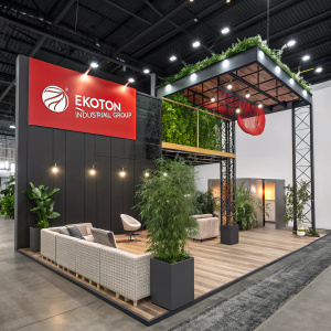 At the trade show, Ekoton Industrial Group's booth features sleek design with tiered setup. Includes comfy seating spots, greenery, and bold red banners showcasing the company logo.
