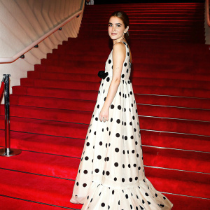 Kiernan Shipka, in a stunning black and white polka dot dress, striking a pose at the Golden Globe Awards. The backdrop features a large red carpet display.