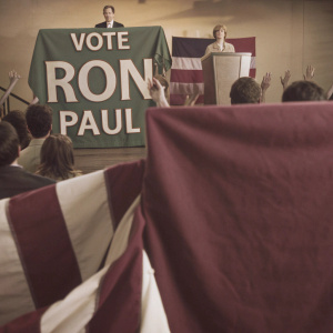 Political rally with Ron Paul supporters. Various banners and signs, including a green background with white text 'VOTE RON PAUL'