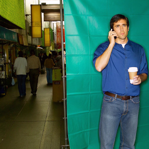 Jake Gyllenhaal, in a casual shirt and jeans, at a bustling outdoor market. Holding a coffee, talking on his phone. Crowded street scene