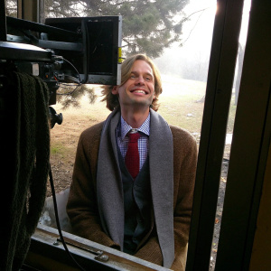 Matthew Gray Gubler, Caucasian, smiling widely. Brown sweater, checkered shirt, red tie, gray scarf. On set of Criminal Minds, behind-the-scenes photo