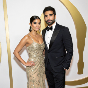 Diane Guerrero and Joseph Ferrera at the Fun Fearless Latina Awards. They are standing in front of a minimalist gold backdrop, both wearing formal attire.