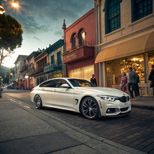 A sleek white BMW 4 Series 430i xDrive Gran Coupe SULEV parked in a vibrant street scene. Pedestrians walking past the gleaming car.