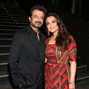 Anil Kapoor and Preity Zinta at the premiere event. Anil in black suit, Preity in vibrant red, brown and geometric patterned dress. They pose against dark, stairway background.