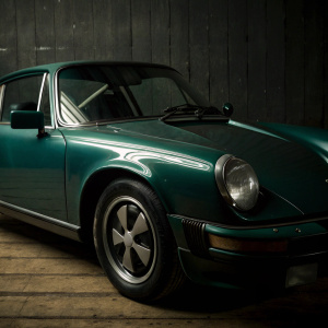 A 1970s era Porsche 911 Carrera in vibrant green. Sleek aerodynamic design with prominent Carrera badge. Dark gray backdrop