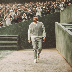 Travis Kelce, wearing Kansas City Chiefs jersey, walking off the field post-game. Crowd cheering in background, photographers capturing the moment
