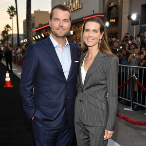 Chris O'Donnell and Caroline Fentress at a Hollywood film premiere. Both are dressed in formal attire. Chris in a navy suit, Caroline in a charcoal pinstripe suit. Crowd of paparazzi in the background.