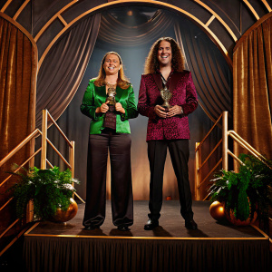 Weird Al Yankovic and Suzanne Krajewski smiling and holding an award at the Comedy Awards Ceremony. Lavish stage backdrop with gold accents