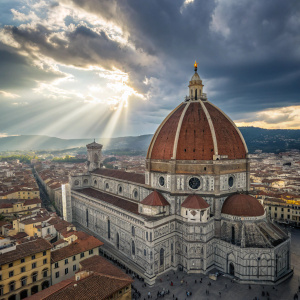 From above, the Basilica di Santa Maria del Fiore, Florence's iconic landmark, spreads its grand wings. The red dome towers over the bustling crowd, a symbol of architectural splendor. Clouds intermittently scatter sunlight, bestowing a magical aura upon the scene's blend of whites, grays, and earthly tones.