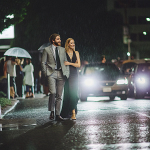 Jake Gyllenhaal and Gwyneth Paltrow walking on a bustling street at night. The vibrant city lights reflecting off the wet pavement.