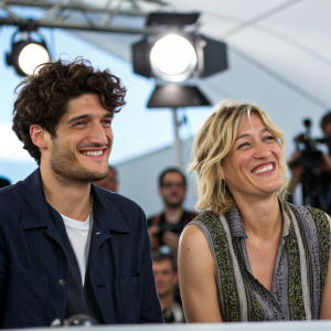 Louis Garrel and Valeria Bruni Tedeschi captured during a press conference. Cheerful expressions, casual attire. Studio lighting, sparse crowd in background