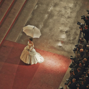 Victoria Abril at Cannes Film Festival. Wearing a stunning white dress with a voluminous skirt. Holding an elegant white umbrella. Surrounded by paparazzi and fans.