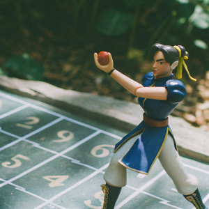 Chun-Li action figure, standing in a fighting pose with an apple. Gray backdrop with white numbers.
