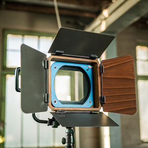 Cinematic camera accessory MatteBox Micro Redrock featured against a dimly lit backdrop with hints of gold and blue hues. The product's sleek design is showcased on an inspiration art & studio blog.