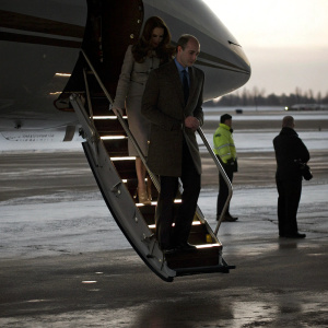 Kate Middleton and Prince William disembarking from a private jet. Snowy tarmac, cold climate, security personnel visible
