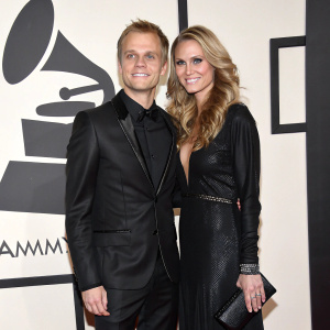 Armin van Buuren and Erika van Thiel at a glitzy awards ceremony. Black attire, white logo backdrop.