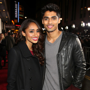 Nareesha McCaffrey, with a radiant smile, wearing a black coat, stands beside Siva Kaneswaran, clad in a gray tunic and leather jacket, at a Hollywood event. Crowded backdrop with flashing lights