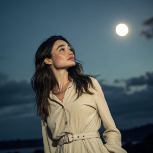 Crystal Reed standing alone under the moonlight. Her face and upper body illuminated softly against a dark sky backdrop.