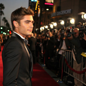 Zac Efron at the premiere of his latest film. Stylish black suit, formal attire. Crowded outdoor setting with flashing cameras and paparazzi