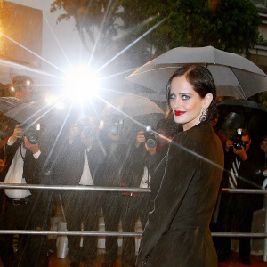 Eva Green, actress, with dark bob haircut, wearing elegant black dress and bold red lipstick, posing for photos at film festival. Crowded venue, flashing lights