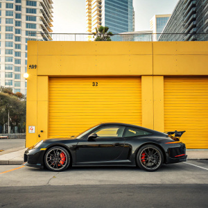 A sleek, black Porsche 911 parked in front of a bright yellow garage door. Sporty car with red brake calipers. Modern urban backdrop