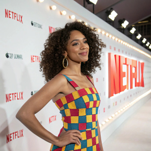 Miriam Morales at the Netflix premiere. Vibrant checkered dress, curly hair, looking directly at the camera. White backdrop, illuminated by soft studio lights