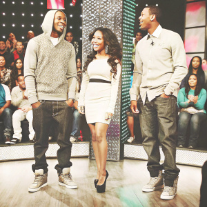 Bow Wow, Keshia Chante, and Marlon Wayans on a vibrant set. Casual yet stylish outfits. Audience laughing and cheering in the background.