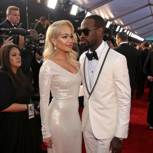Rita Ora and Juicy J at the annual Grammy Awards. Rita in a shimmering white gown, Juicy J in a sharp tuxedo. Crowded red carpet scene