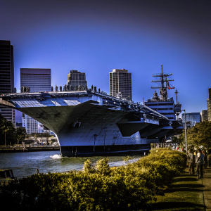 The USS Intrepid, a historic aircraft carrier, now docked in San Francisco Bay. Surrounded by modern skyscrapers and vibrant city life.