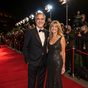 James Nesbitt and Sonia, elegantly dressed, surrounded by flashing camera lights at a gala event.