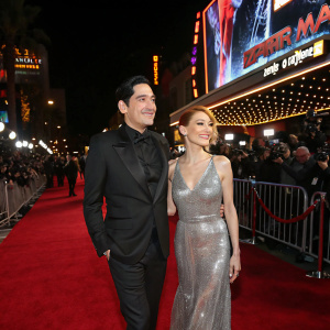 David Dastmalchian, wearing a black tuxedo, and Evelyn Leigh, in a silver sequined gown, walk on the bustling Hollywood red carpet for the Spider-Man: No Way Home premiere.