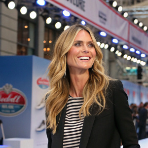Heidi Klum at a promotional event for Dr. Scholl's DreamWalk shoes. Cheerful expression. Wearing a black blazer and a striped shirt. Long, wavy blonde hair.