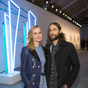 Diane Kruger and Jared Leto attending an art exhibition opening. Modern art installations and bright lights in the background.