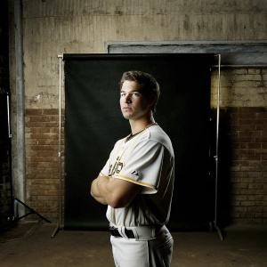 Alex Kirilloff, baseball player, in a professional studio. White baseball jersey with team logo, focused expression. Blue-toned backdrop. Soft lighting emphasizing face and uniform details.