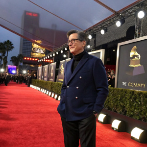 Stephen Colbert, in a navy blue blazer, stands confidently at the Grammy Awards. Red carpet backdrop